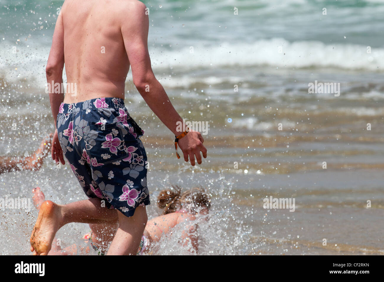 Les personnes en cours d'exécution dans la mer à la plage de Fistral. Banque D'Images