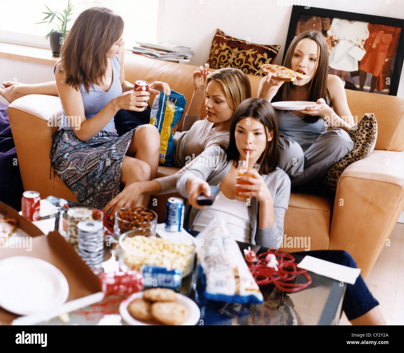 Groupe d'adolescents de sexe féminin assis sur un canapé, mangeant et buvant la malbouffe regarder la télévision Banque D'Images