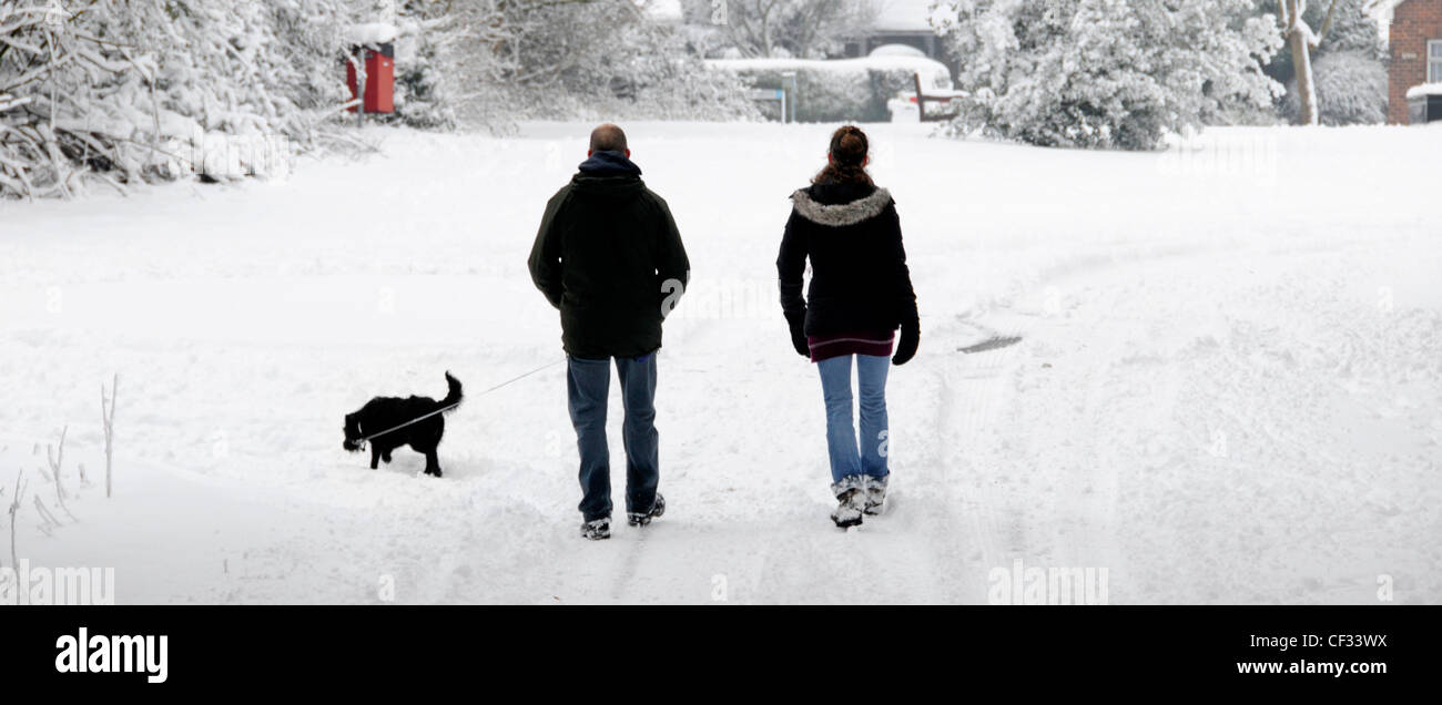 Marcher sur la couverture de neige le long de la route de campagne un homme et une femme couple faisant la promenade de chien du matin après de fortes chutes de neige d'hiver Brentwood Essex Angleterre Royaume-Uni Banque D'Images