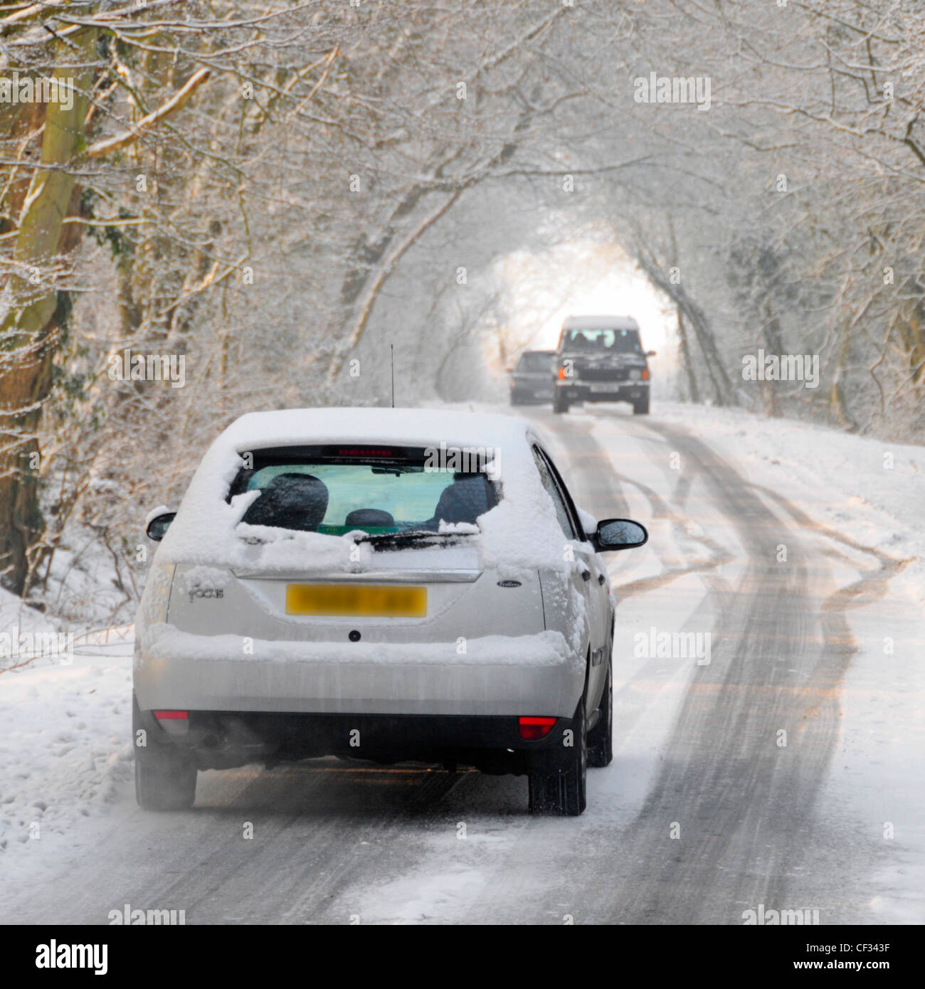Vue arrière voiture Ford Focus qui laisse la place à la conduite le long de la route de campagne enneigée bordée d'arbres à proximité de la circulation venant en sens inverse hiver Essex Angleterre Royaume-Uni Banque D'Images