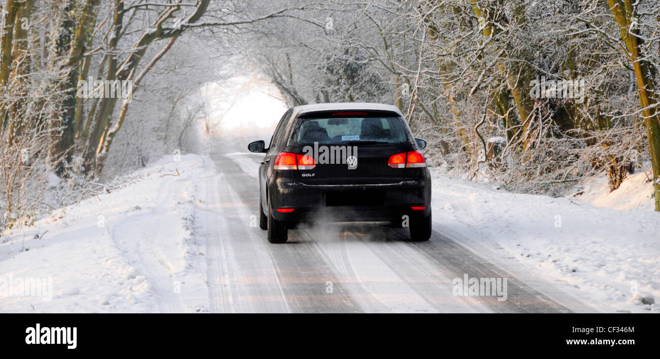 Paysage d'hiver & Volkswagen voiture roulant lentement à travers bois blanc le long de la campagne couverte de neige glacée route étroite Brentwood Essex England UK Banque D'Images