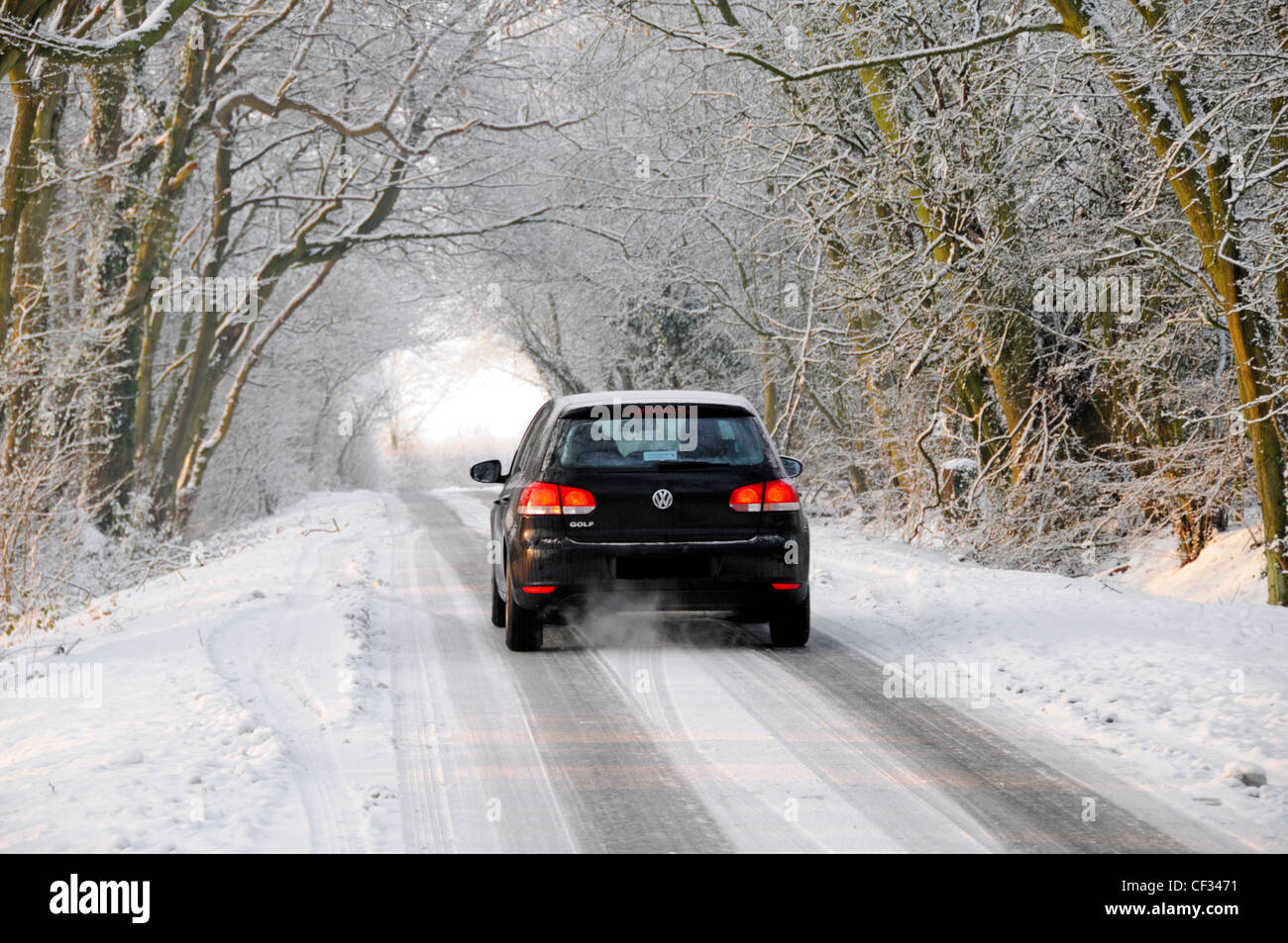 L'hiver est magnifique VW Volkswagen Golf voiture conduite sur neige Et route couverte de glace à travers l'arcade des arbres blancs d'Essex Angleterre Royaume-Uni Banque D'Images