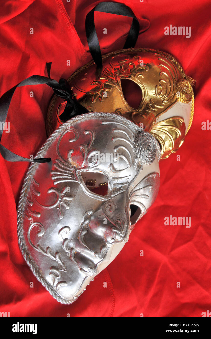 Deux d'argent et d'or théâtre de masques colorés contre satiné rouge. Banque D'Images