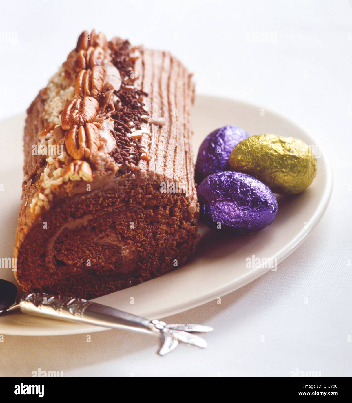 Le thé de pâques suisse Swiss roll roll on plate surmontée d'écrous, avec cuillère en argent et feuilles couvertes des œufs en chocolat Banque D'Images