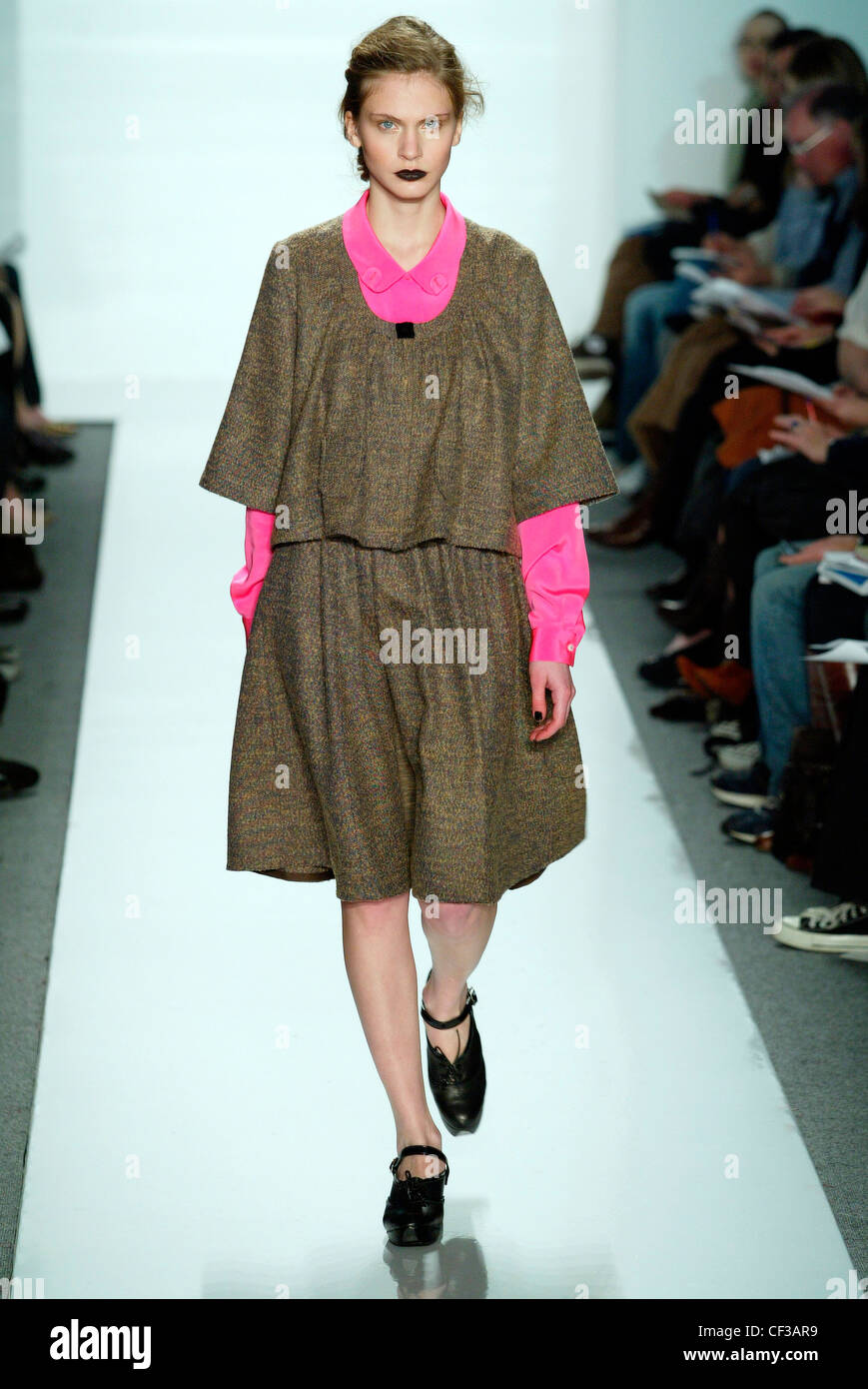 Blonde portant une robe vert armée sur une chemise rose chaud et chaussures noires. Banque D'Images