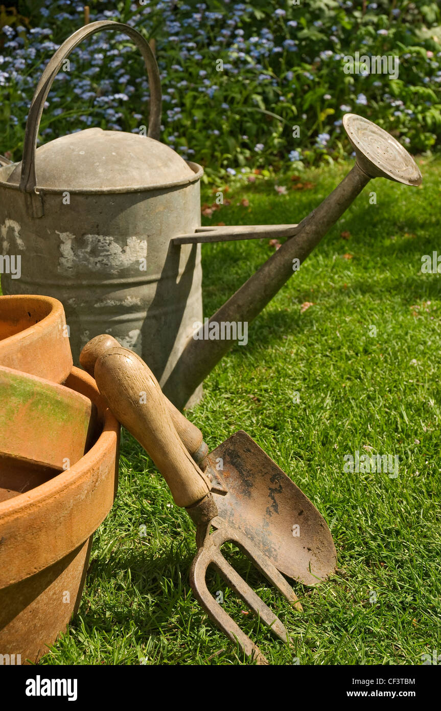 Arrosoir en zinc, truelle, fourchette et pots en argile dans le jardin. Banque D'Images
