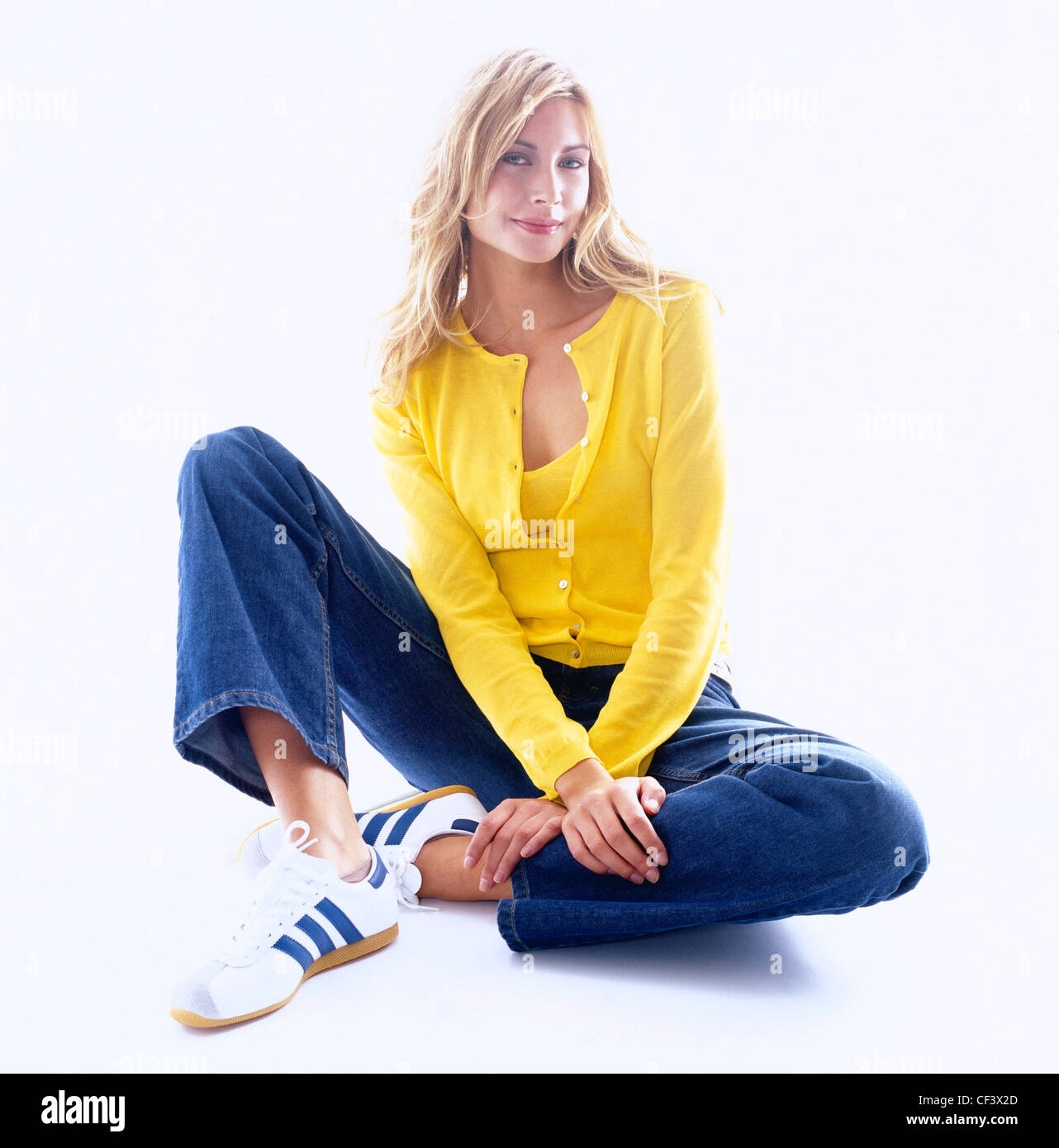 Denim Femme longue chevelure blonde wearing cardigan jaune sur jaune vest top, bleu denim jeans bleu et blanc adidas formateurs Banque D'Images