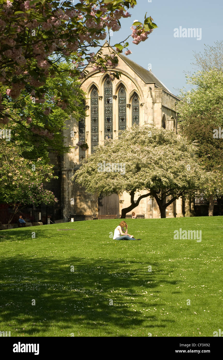 Une jeune femme assise sur l'herbe la lecture d'un livre à l'extérieur de la Bibliothèque du doyen de la cathédrale dans le parc. Banque D'Images