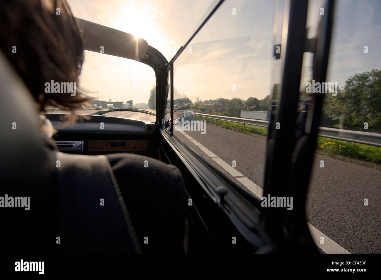 La conduite dans le siège passager d'une voiture décapotable classique sur l'autoroute vers le soleil de l'après-midi Banque D'Images