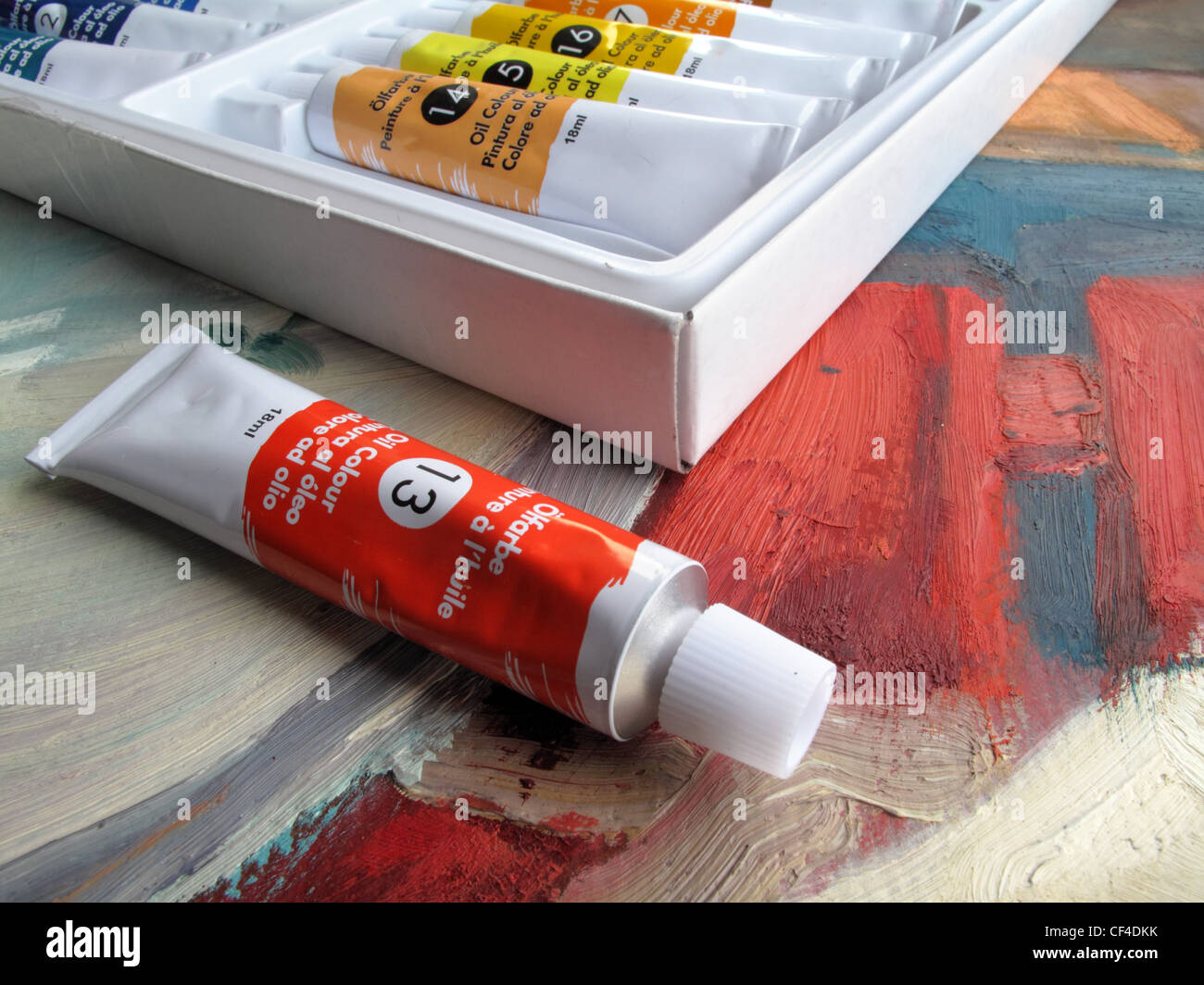 Un nouveau tube de peinture à l'huile rouge est assis à côté d'une boîte de peinture à l'huile - se trouvent sur le dessus d'une peinture à l'huile. Banque D'Images