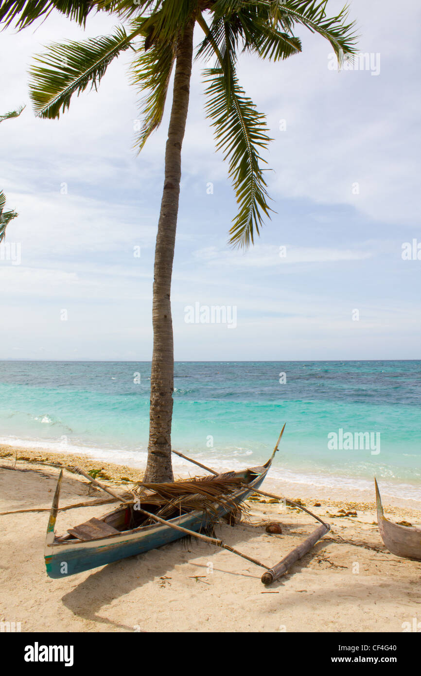 Un petit bateau se repose à l'ombre d'un palmier sur une plage de l'île à distance Banque D'Images