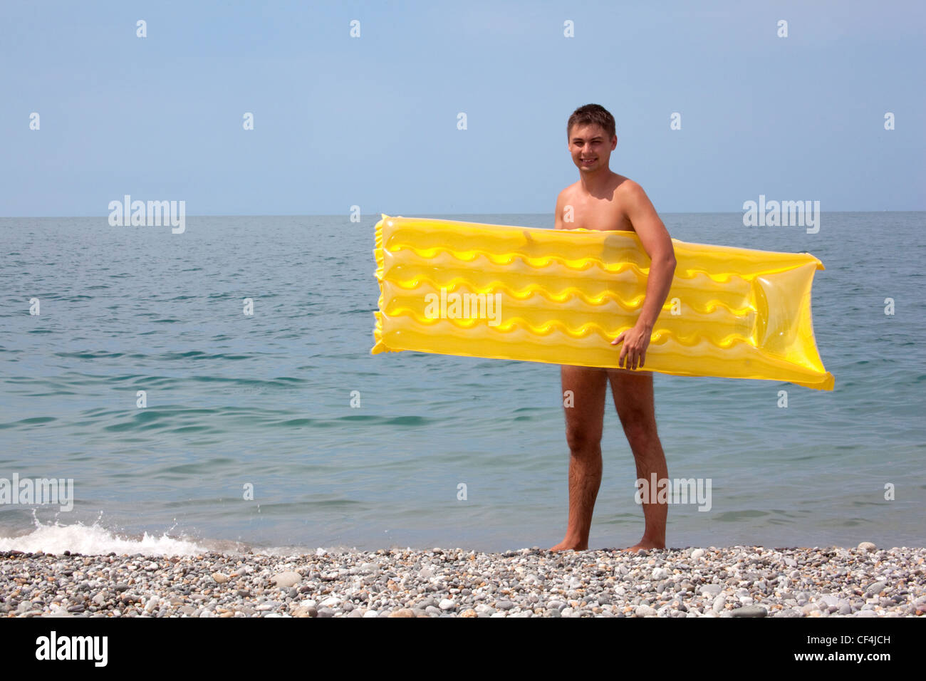 Jeune mec avec matelas jaune sur le littoral. L'homme se dresse sur une plage de galets Banque D'Images