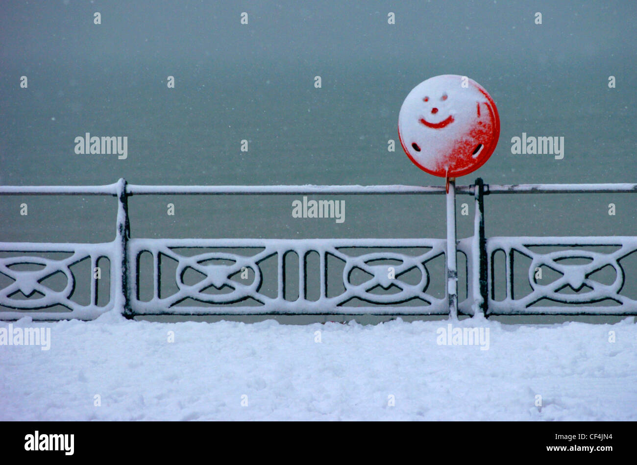 Un smiley dessiné dans la neige recouvrant un panneau rouge sur le front de mer de Brighton. Banque D'Images