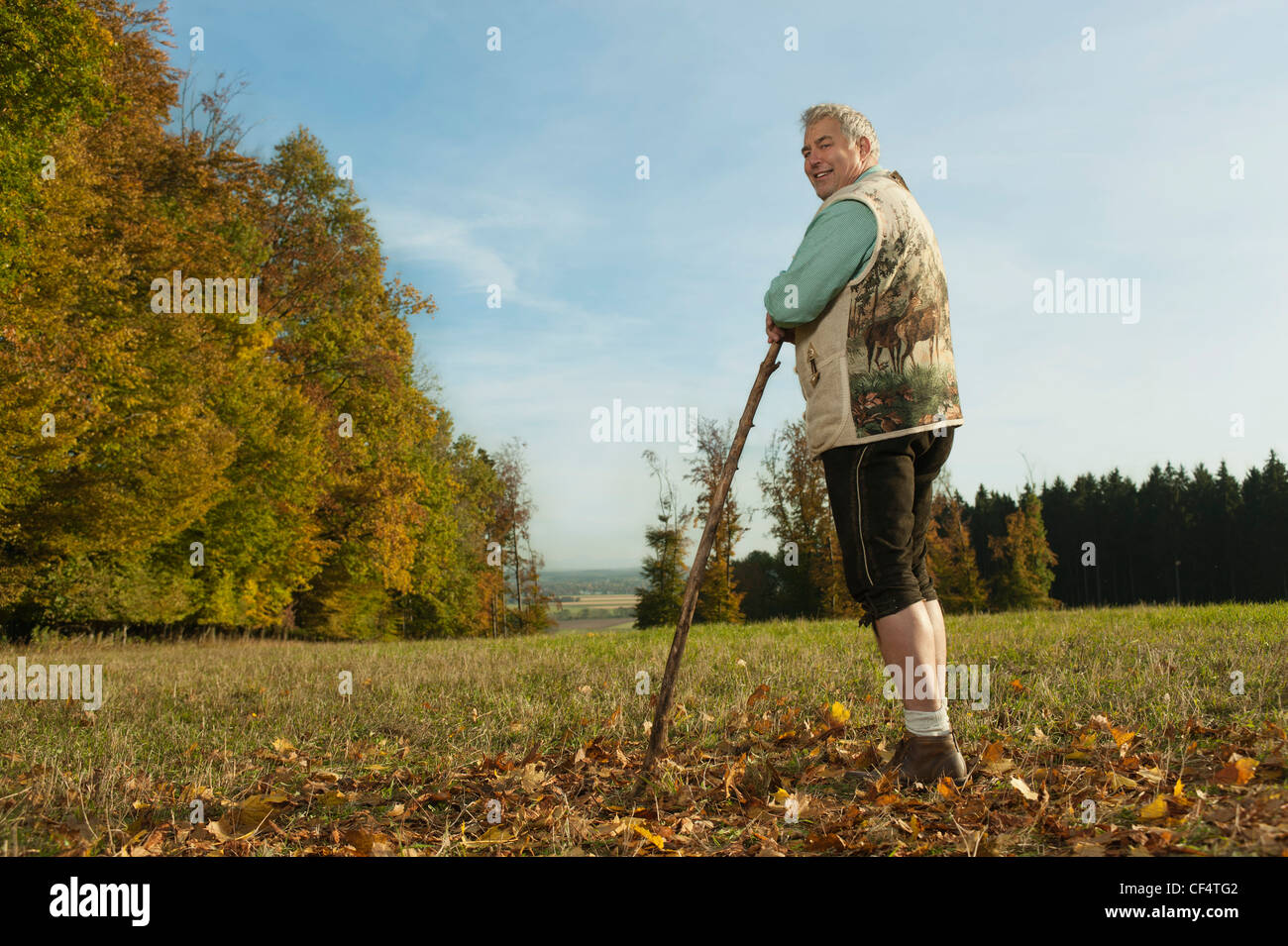 Germany, Bavaria, Mature man in traditional gilet avec canne, smiling, portrait Banque D'Images