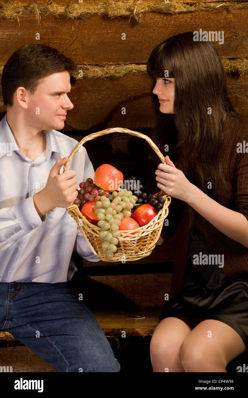 L'homme souriant et jeune femme avec panier de fruits assis sur un banc en bois en log hut, Close up Banque D'Images