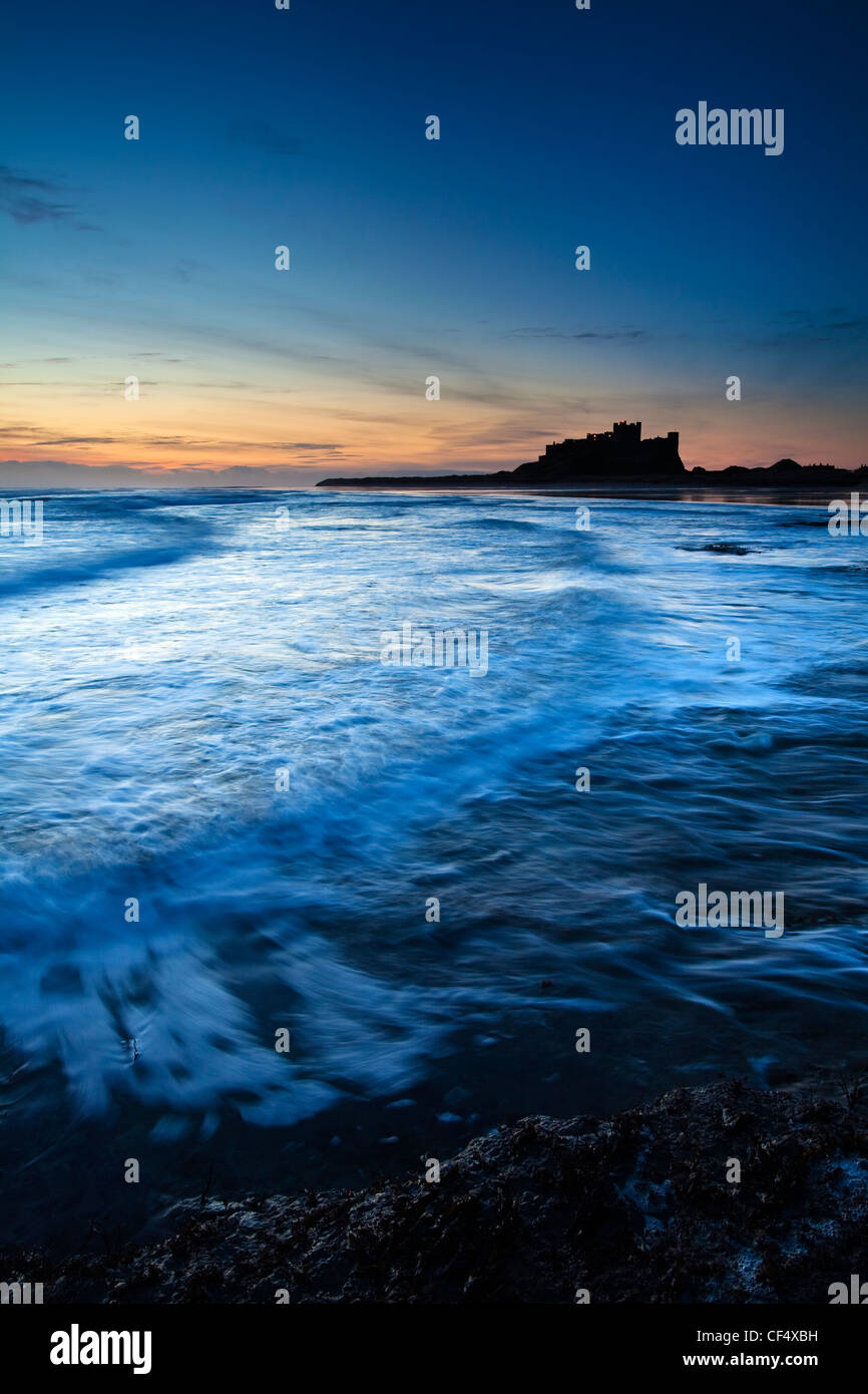 Vagues roulant sur la plage par Château de Bamburgh, à l'aube. Banque D'Images