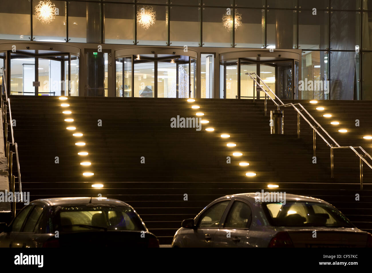 Grande entrée dans immeuble de bureaux modernes dans la nuit, deux voitures sur le parking Banque D'Images