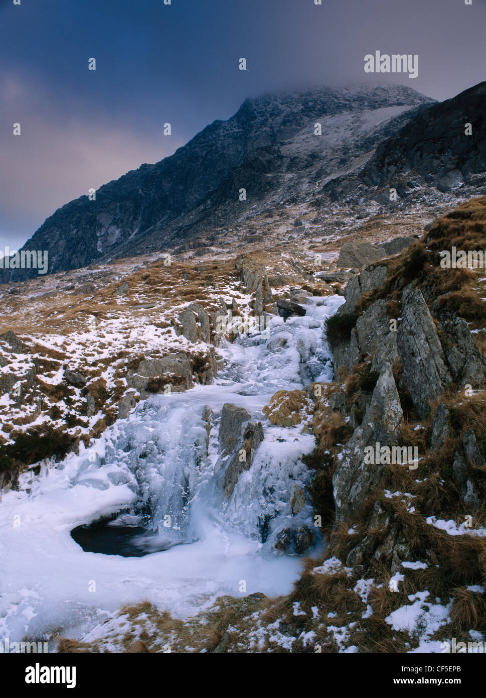 Petite cascade et bassin gelé en partie sur un ruisseau qui coule à Bochlwyd de Llyn Llyn Ogwen. La masse sombre de Tryfan est bey Banque D'Images