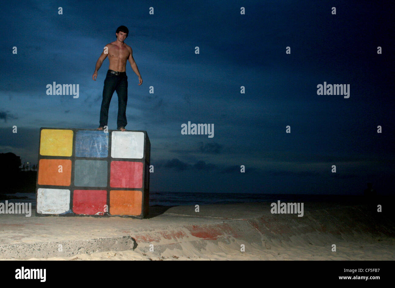 Homme avec cheveux brune, portant jean noir, debout sur le Rubik's Cube, souriant, regardant Dylan Walker Banque D'Images