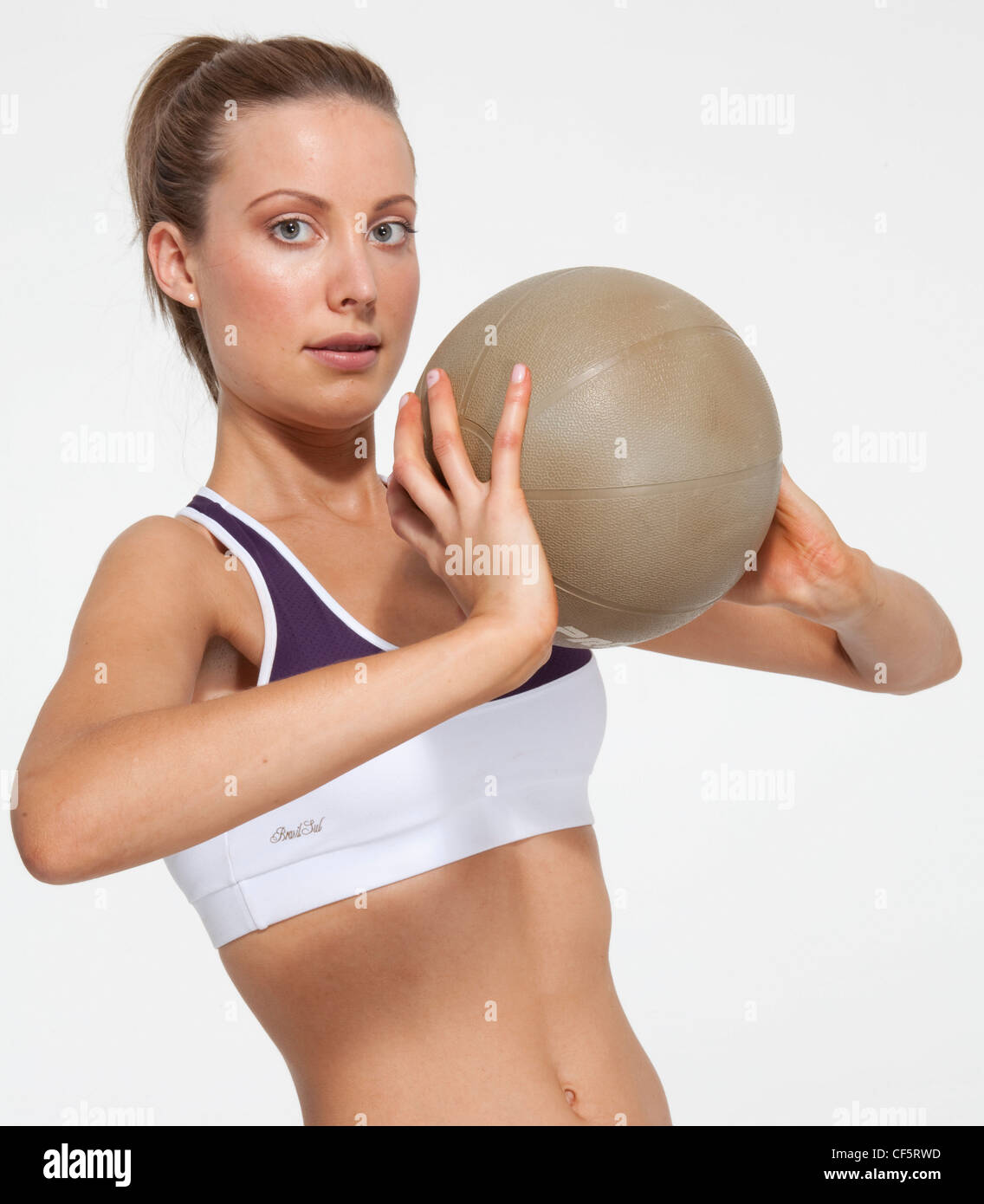 Attacher les cheveux juste femelle en queue de cheval, portant un gilet recadrée, tenant un ballon, les deux mains à sa poitrine, souriant, Banque D'Images