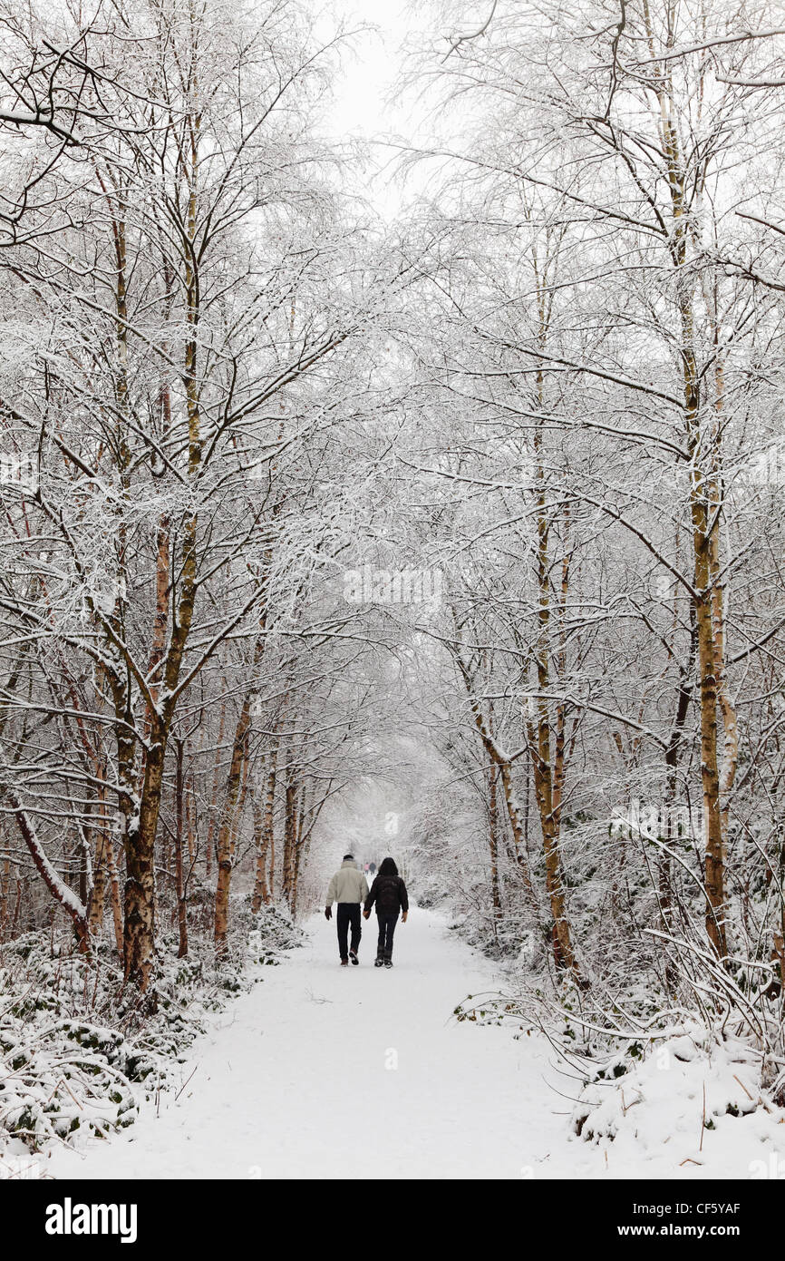 Un couple marche main dans la main le long d'un chemin à travers des arbres couverts de neige. Banque D'Images