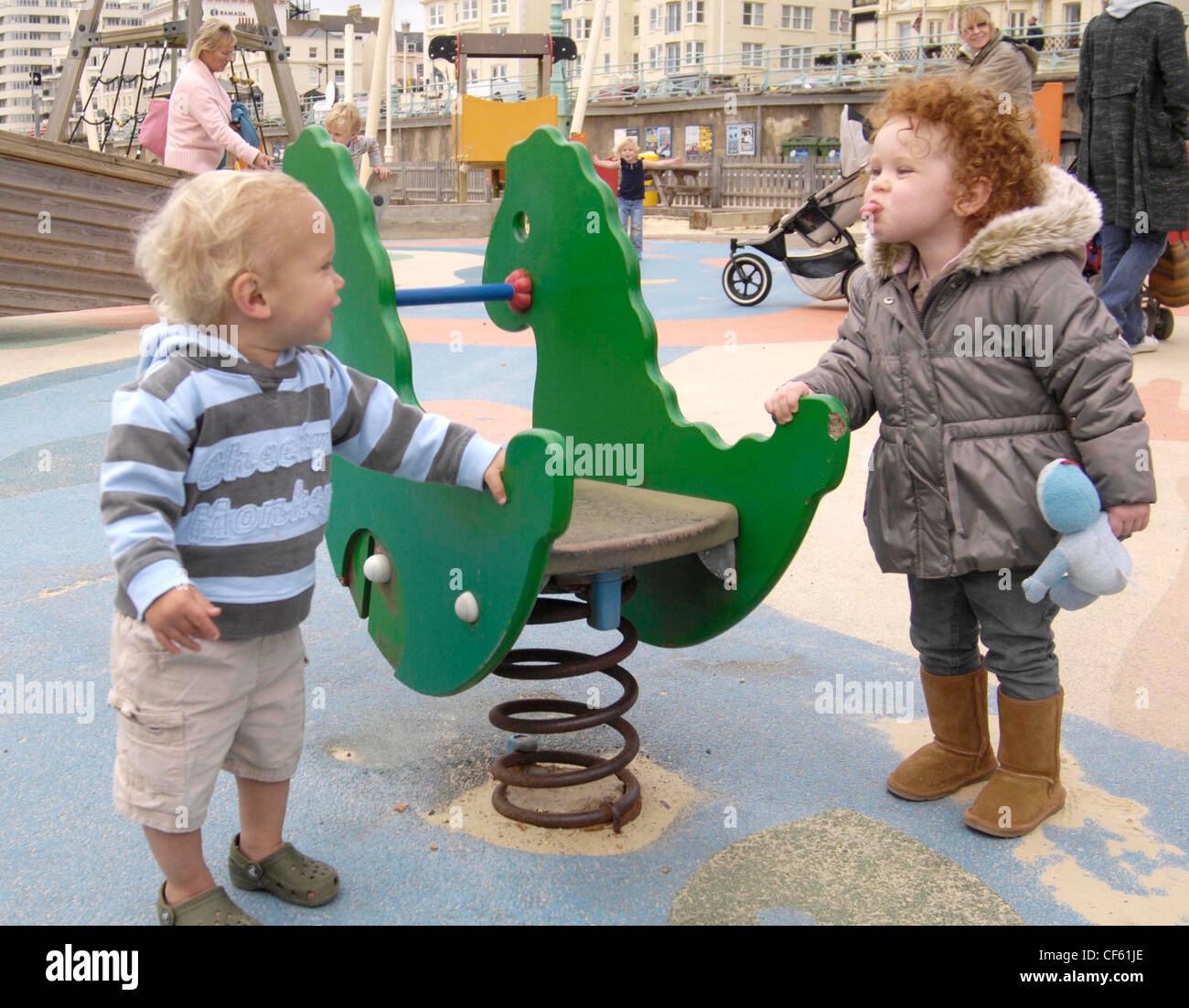 Enfant de sexe féminin, les cheveux bouclés brun rouge portant la veste, jeans gris et marron bottes UGG, tenant un dinosaure vert sur ressort à Banque D'Images