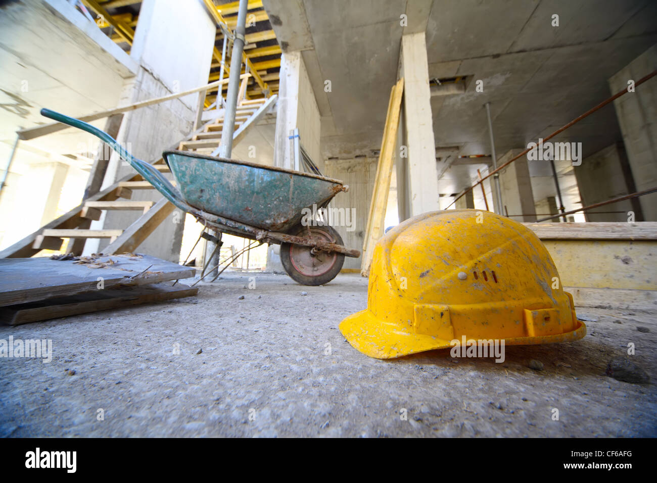 Casque jaune et petit panier sur le sol en béton à l'intérieur de bâtiment inachevé Banque D'Images