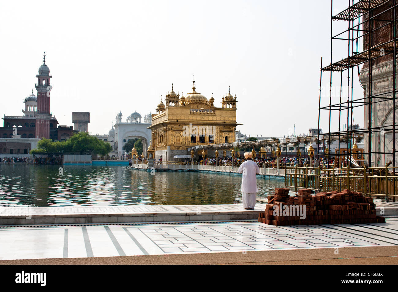 Priant au bord de l'étang à l'intérieur du temple d'Or, compte tenu de l'Amrit Sarovar, Darbar Sahib et pont-jetée au-dessus de l'eau Banque D'Images