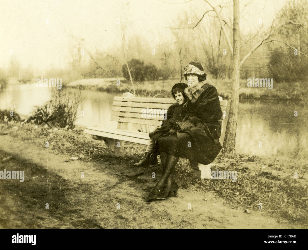 Femme et enfant assis sur un banc à côté du petit ruisseau river fashion women's robe noire collant High heels 1900s 1800s vintage Banque D'Images