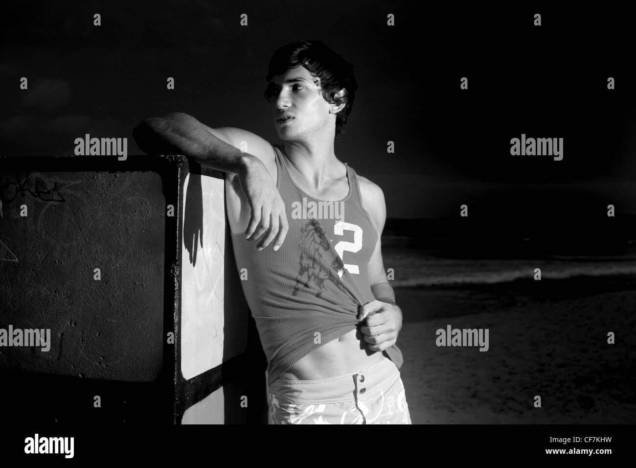 Brune, les cheveux des hommes en short et gilet, debout sur la plage, s'appuyant contre le Rubiks Cube, souriant, à la recherche de la Banque D'Images