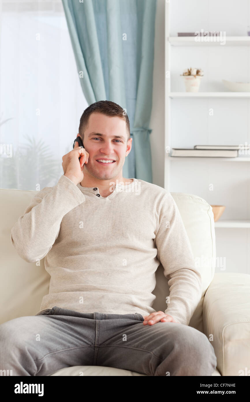 Portrait d'un jeune homme au téléphone alors qu'il était assis sur son canapé Banque D'Images