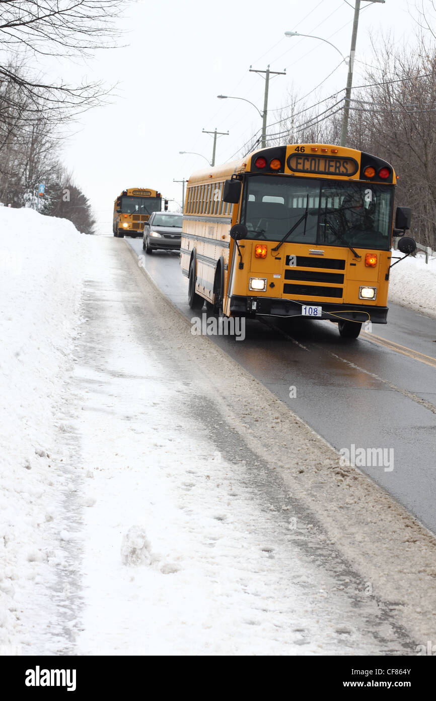Deux autobus scolaires et une voiture de la conduite sur route en hiver Banque D'Images