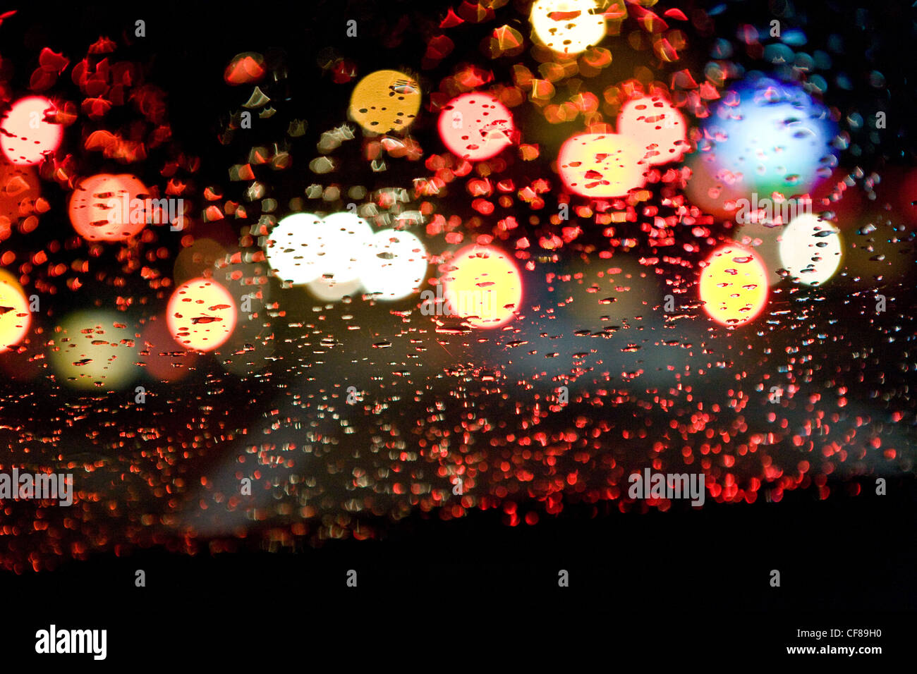 Vue à travers le pare-brise de voiture humide, trafic, nuit, ville. Banque D'Images
