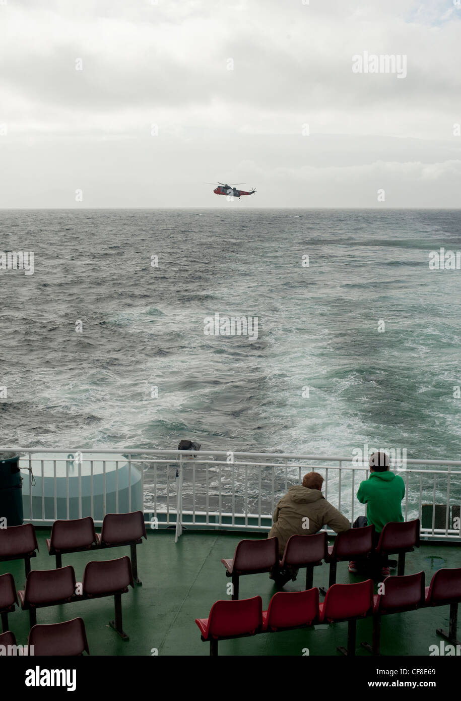 Un hélicoptère Sea King de la RAF en vol stationnaire au-dessus de la mer que deux passagers du traversier de regarder sur le bateau en Écosse. Banque D'Images