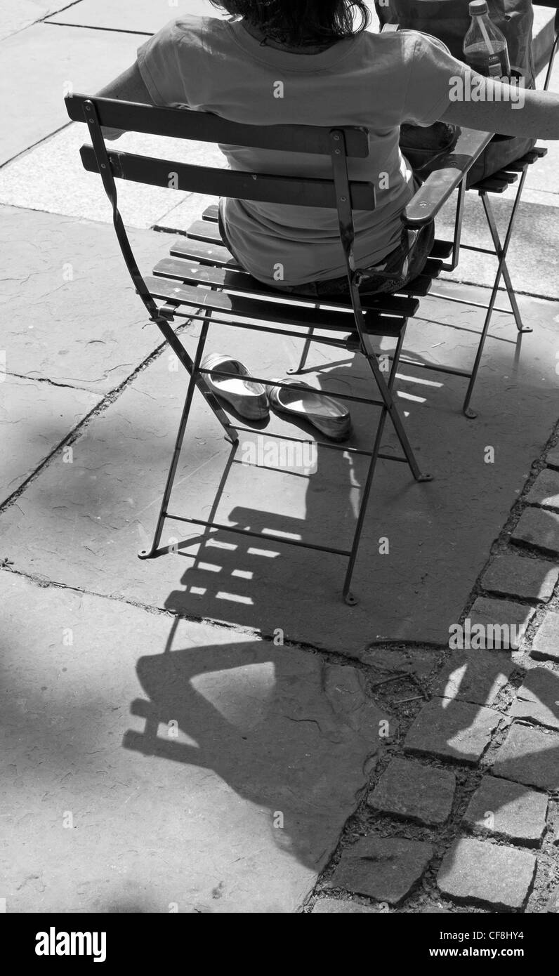 Une femme en Bryant Park se détend comme le matin soleil projette son ombre sur la chaussée. Banque D'Images