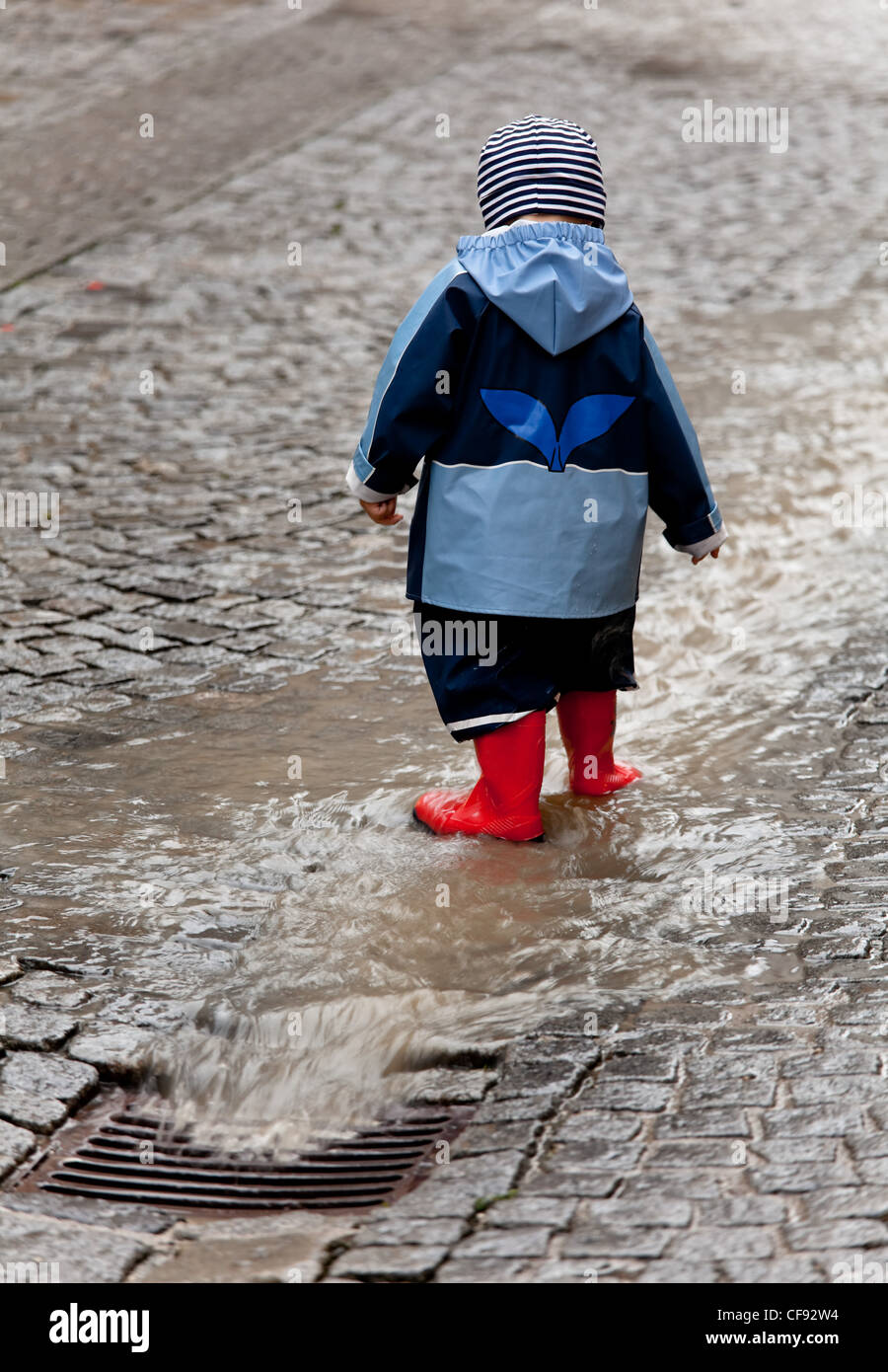 Enfant avec des vêtements de pluie et avoir du plaisir à jouer sous la pluie Banque D'Images