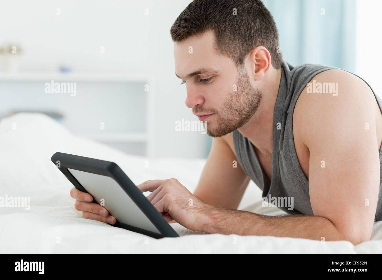 Bel homme à l'aide d'un ordinateur tablette en position allongée sur le  ventre Photo Stock - Alamy