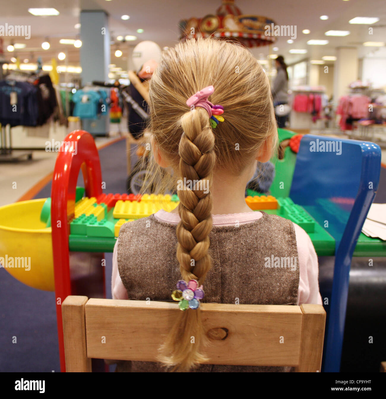 Enfant de sexe féminin, juste en haut et rose robe brune, assis à la table morceaux de Lego devant elle à la jouer Banque D'Images