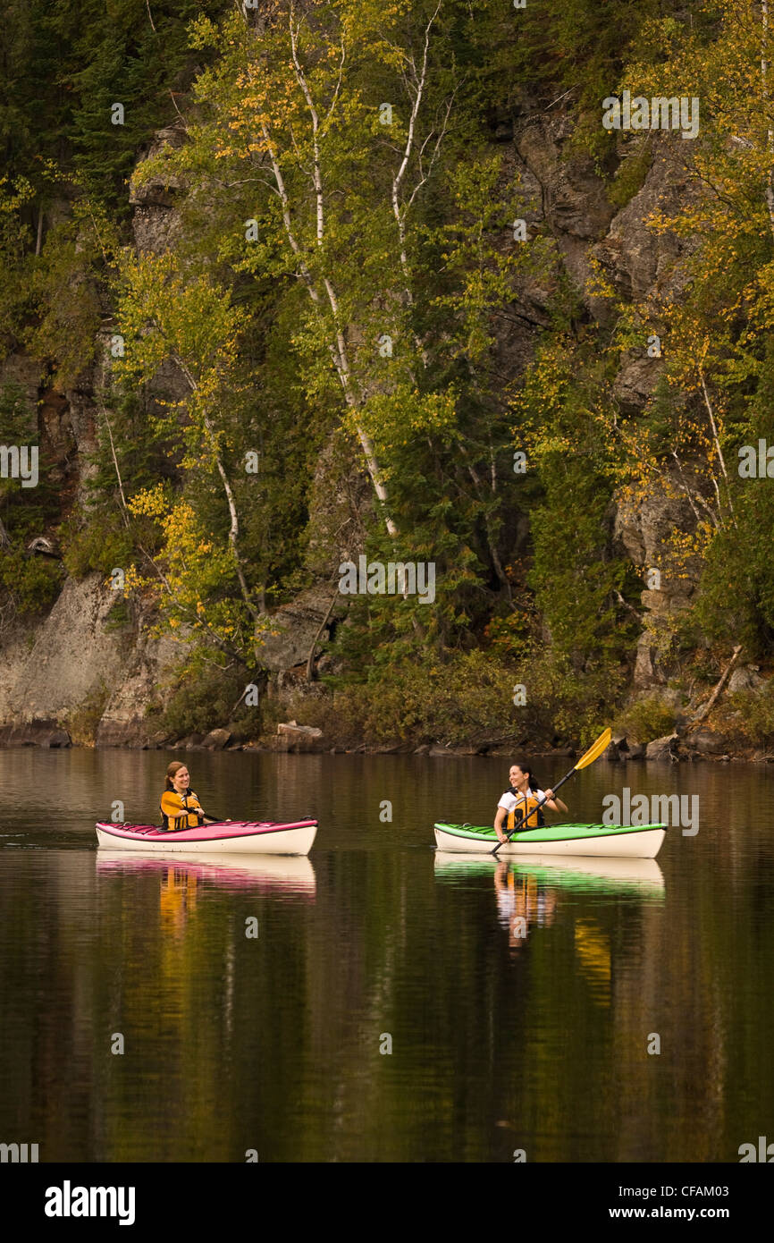 Deux jeunes femmes kayaking on Oxtongue Lake en automne, Mukoka, Ontario, Canada. Banque D'Images