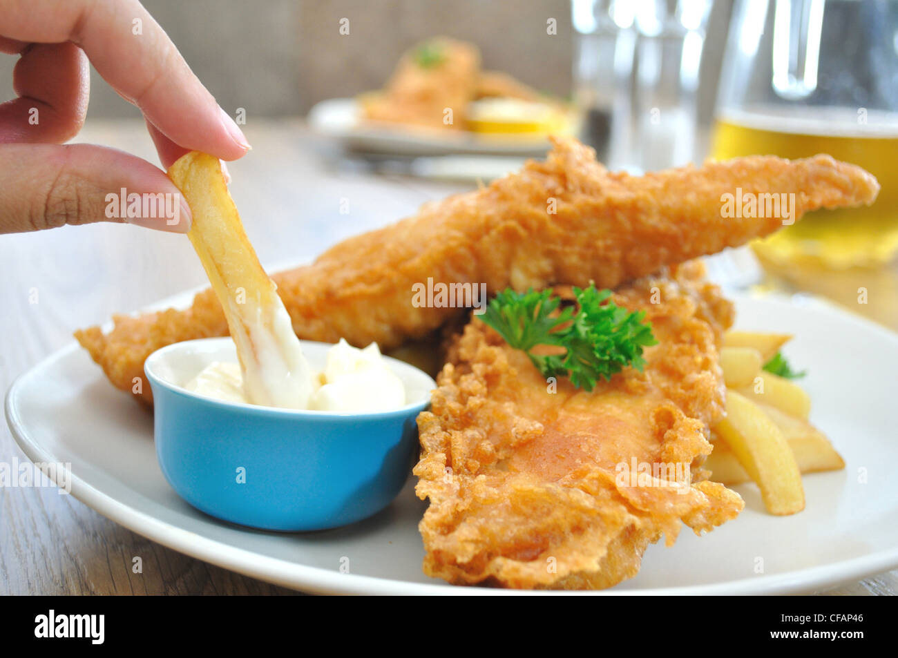 Chip étant plongé dans la mayonnaise sur une plaque avec des filets de morue battue croustillants Banque D'Images