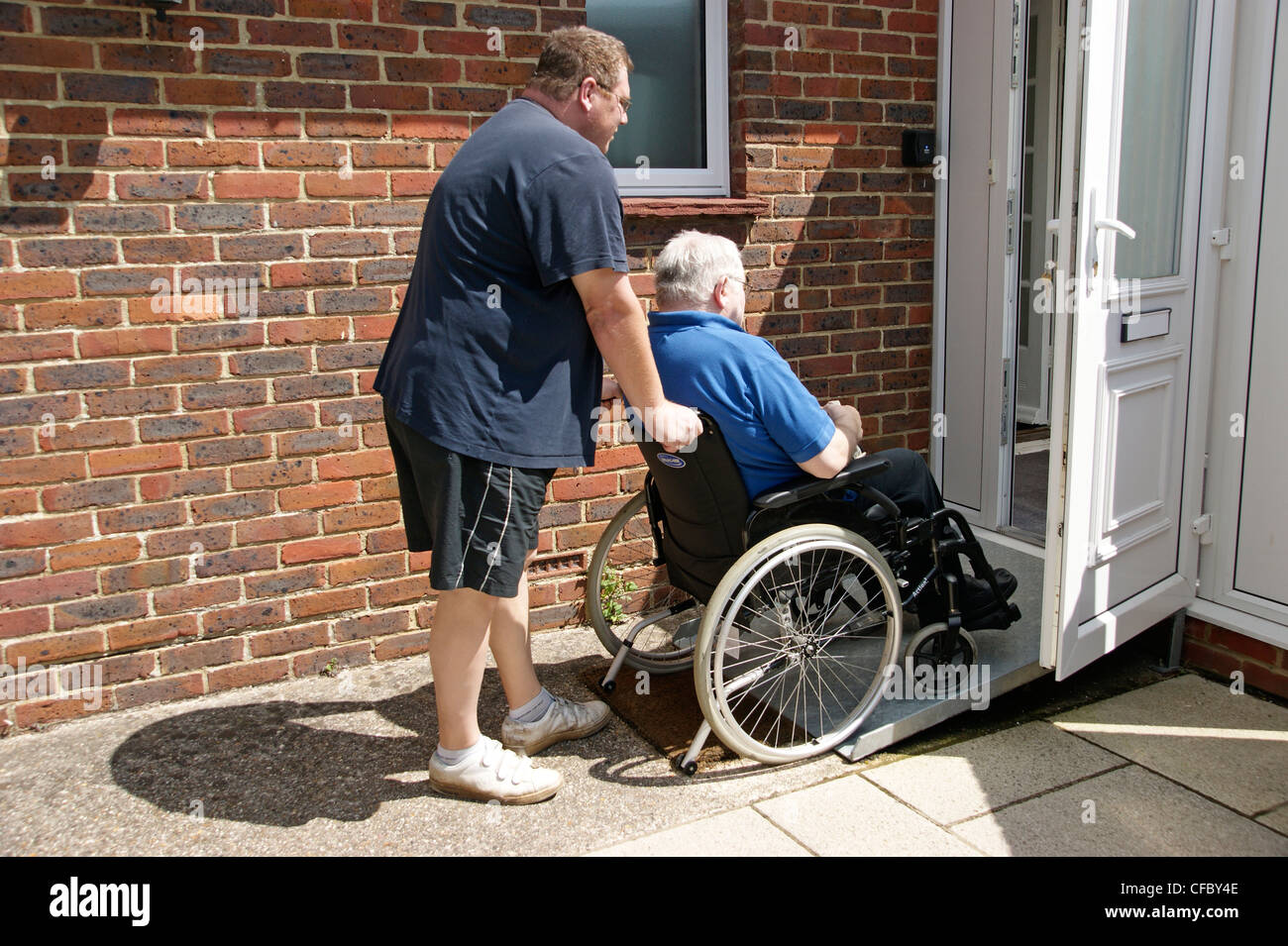 Carer mâle / son poussant un homme âgé en fauteuil roulant sur la rampe d'accès à la propriété Banque D'Images