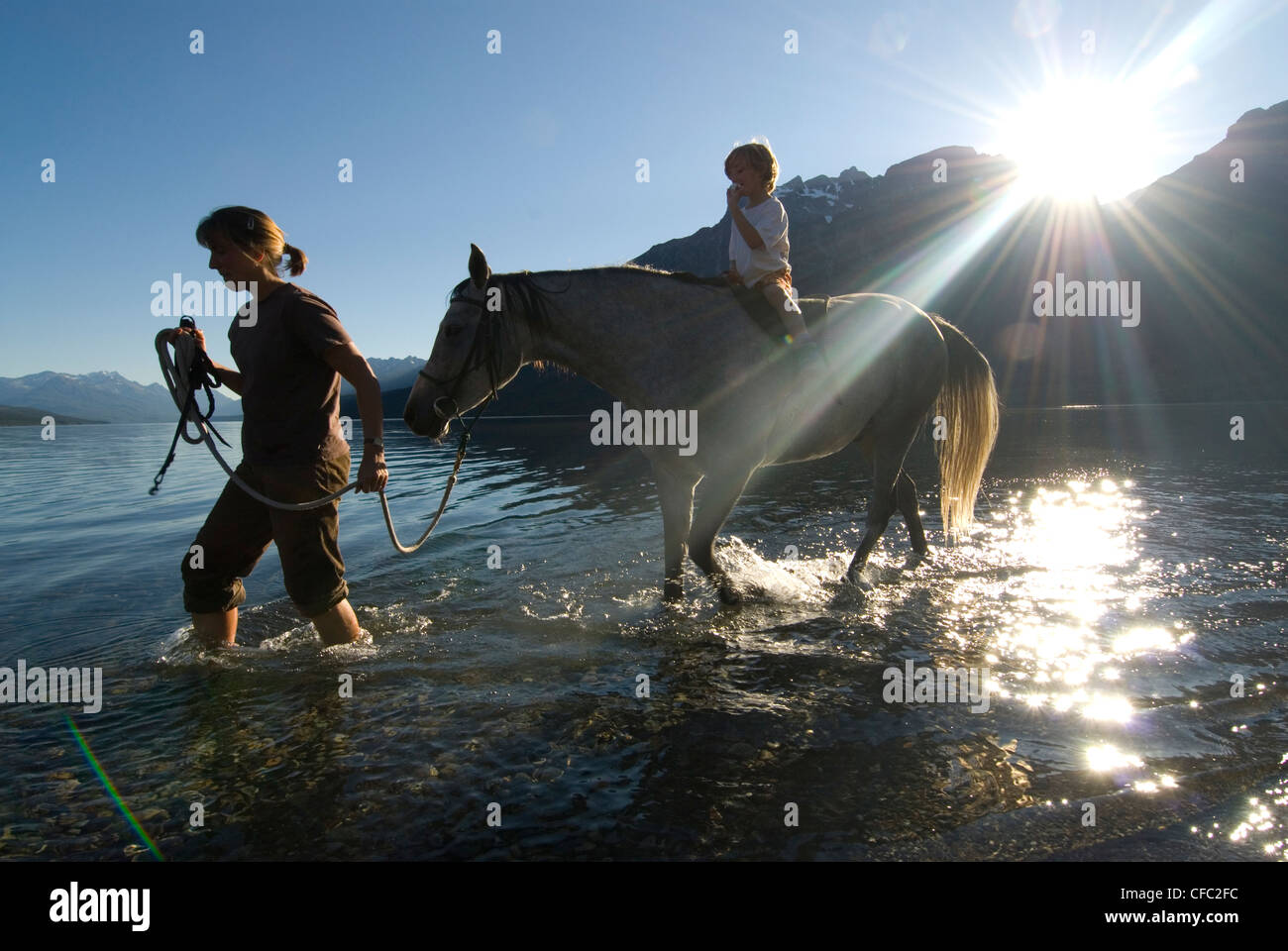 Les traits d'une femme son fils sur un cheval dans les eaux peu profondes de Tatlayoko Lake, British Columbia, Canada Banque D'Images