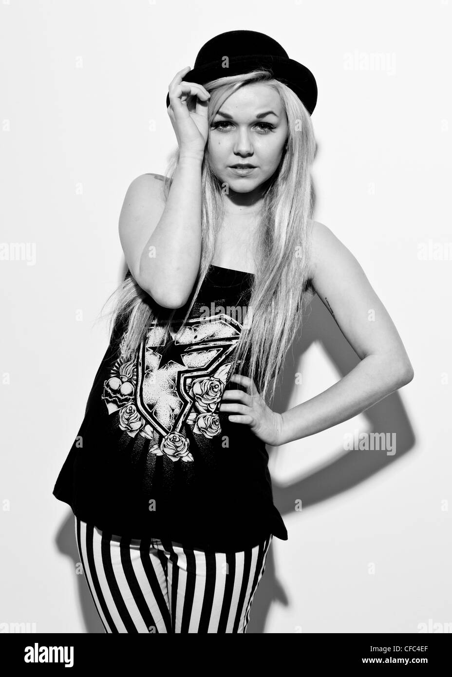 Demi-longueur noir et blanc studio portrait de femme sur fond blanc portant des jeans noir et blanc et noir chapeau melon Banque D'Images