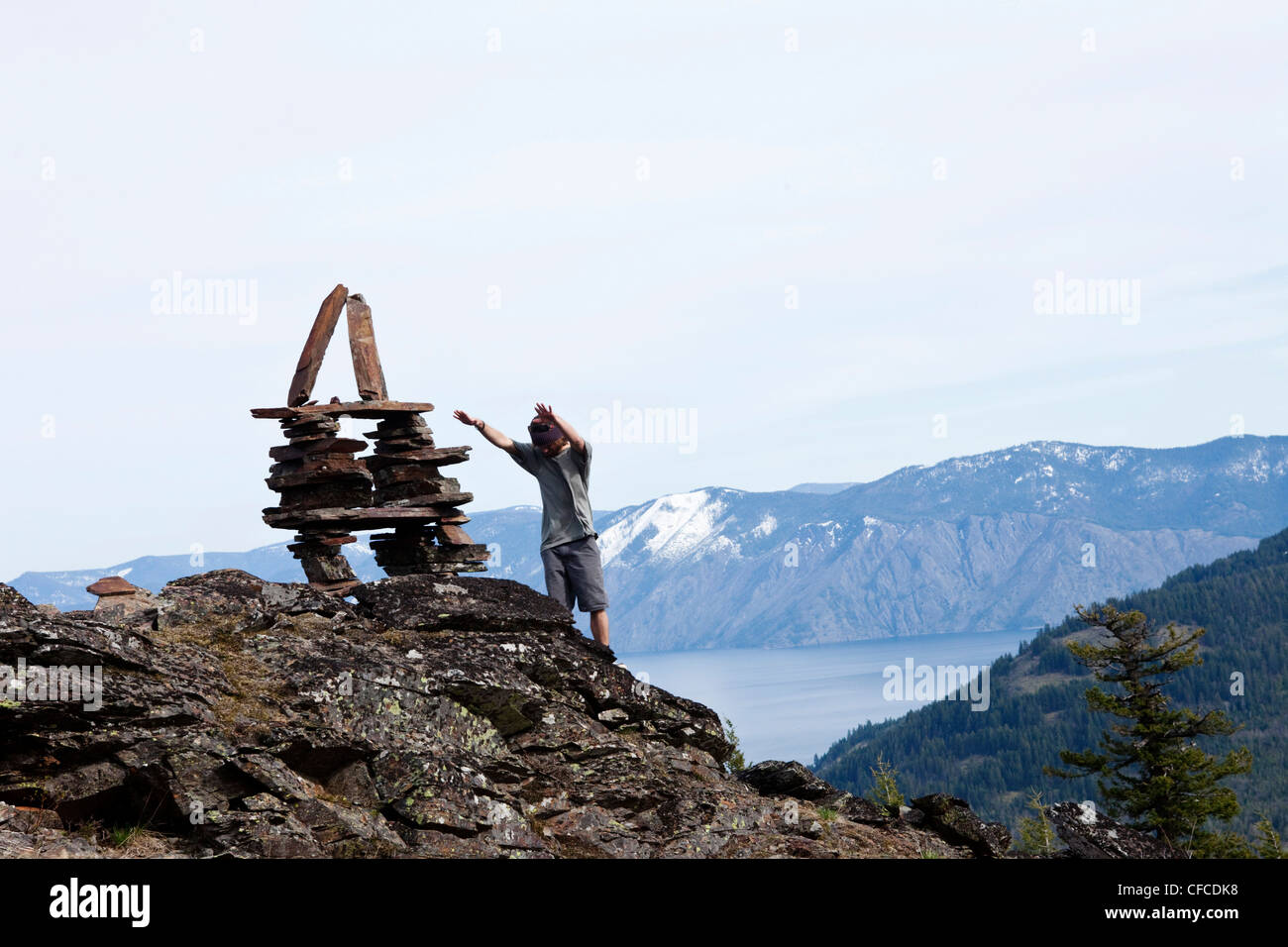 Un jeune homme prie à côté d'un grand cairn au-dessus d'un lac de montagne dans l'Idaho. Banque D'Images