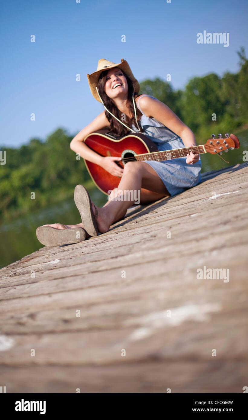 Une jeune femme est assise sur un quai à jouer de la guitare. Banque D'Images