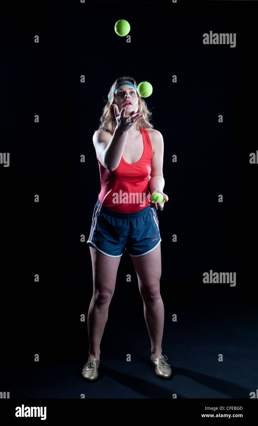 Athlète féminine rétro Goofy jongle avec 3 balles de tennis devant un fond noir. Banque D'Images