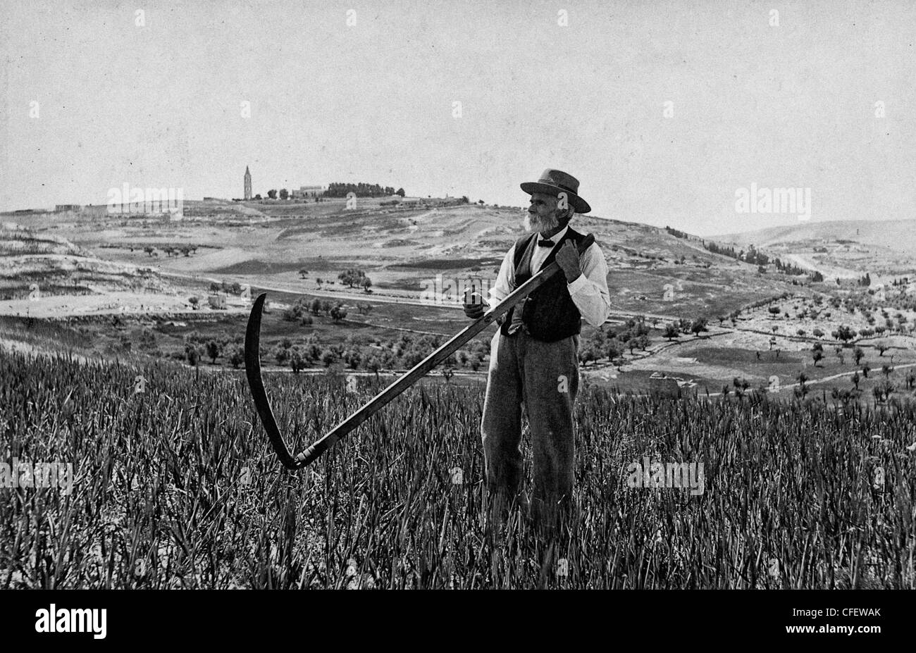 Colonie américaine états Josef Larsson, standing in field sur le Mont Scopus, tenant une faux et Jérusalem, vers 1920 Banque D'Images