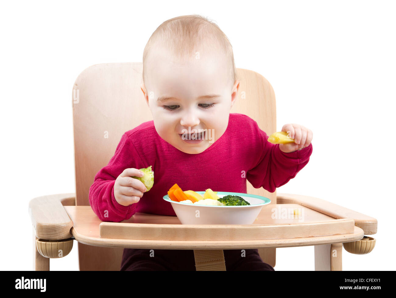 Jeune enfant en chemise rouge manger des légumes dans la chaise en bois. Banque D'Images