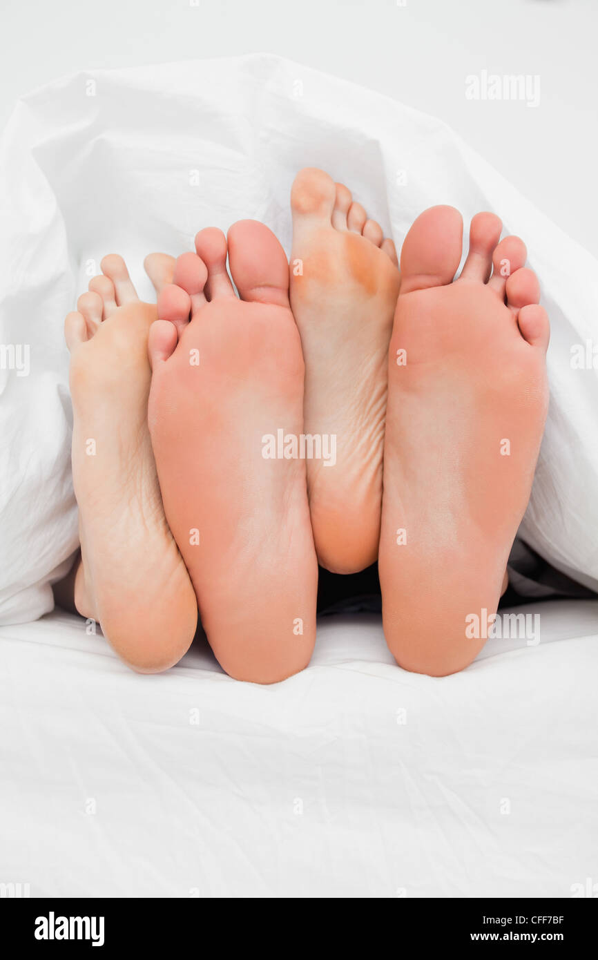 Close up, deux paires de pieds dans le lit croisés sur chaque autre Banque D'Images