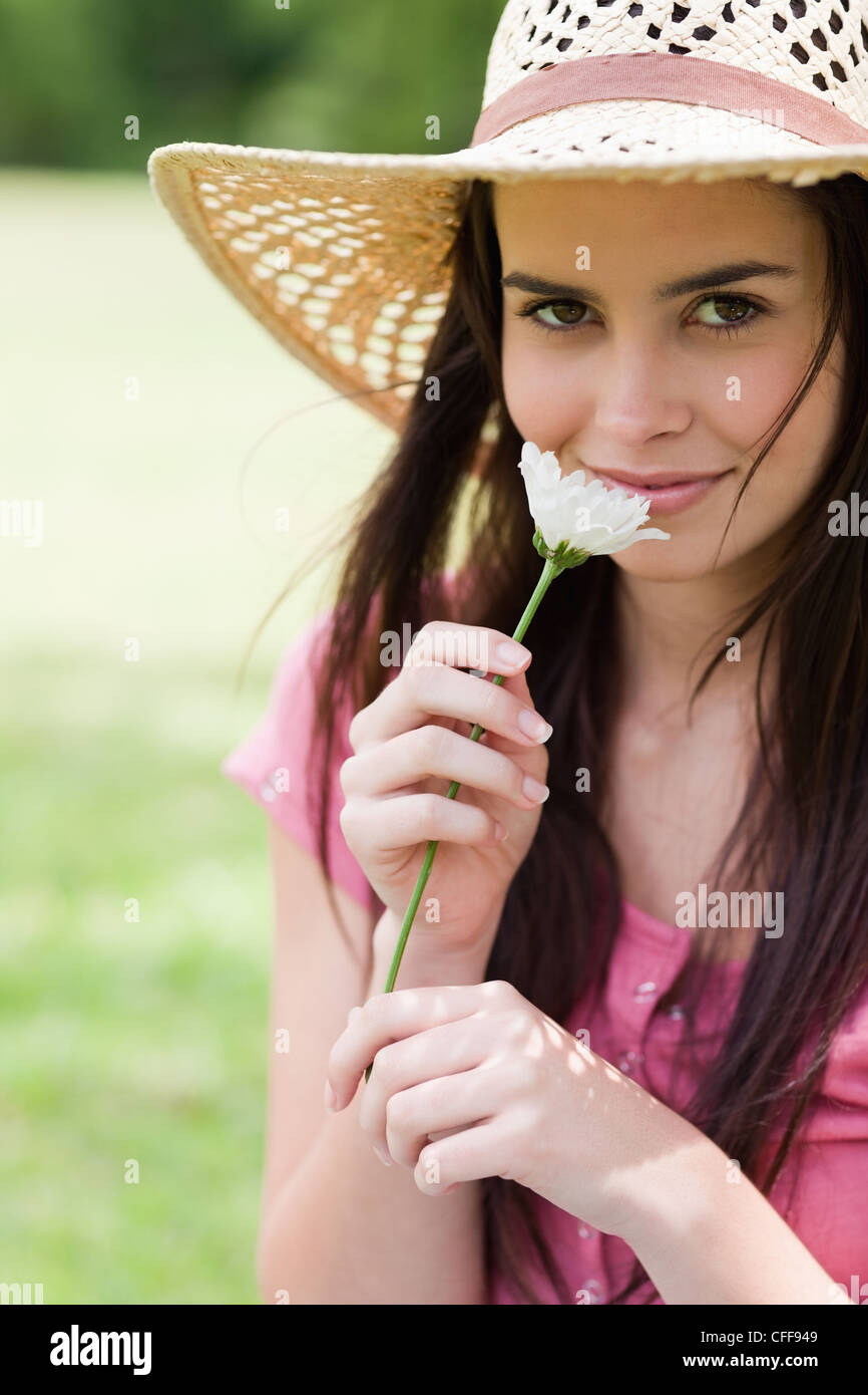 Jeune fille paisible qui sent une fleur tout en se tenant dans un parc avec un chapeau de paille Banque D'Images